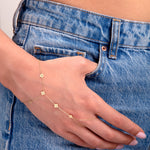 Hand harness bracelet with small 14k gold floral charms on a woman's hand in denim jeans

