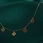 14K gold necklace featuring multiple four-leaf clover charms, styled on deep green satin background.