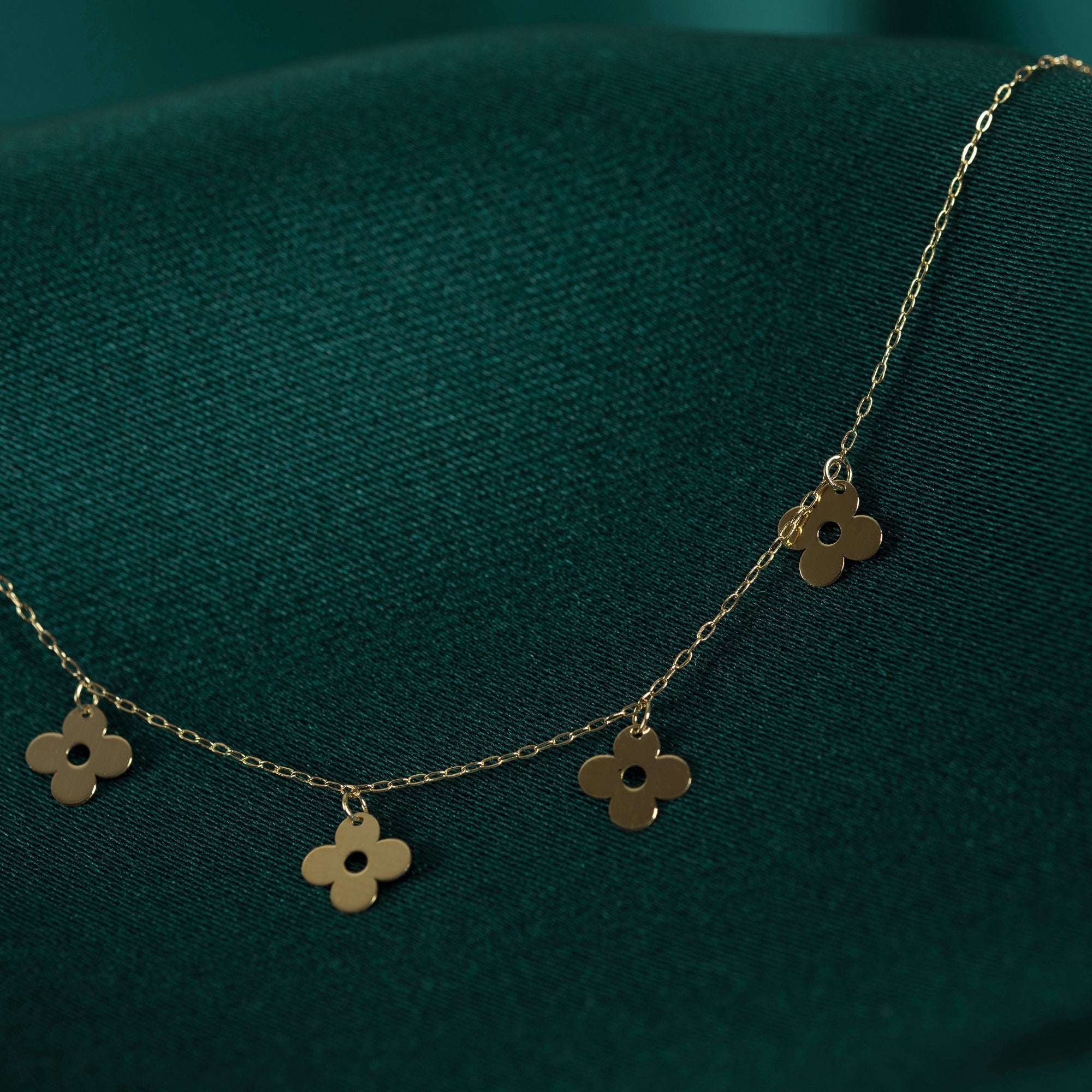 14K gold necklace featuring multiple four-leaf clover charms, styled on deep green satin background.