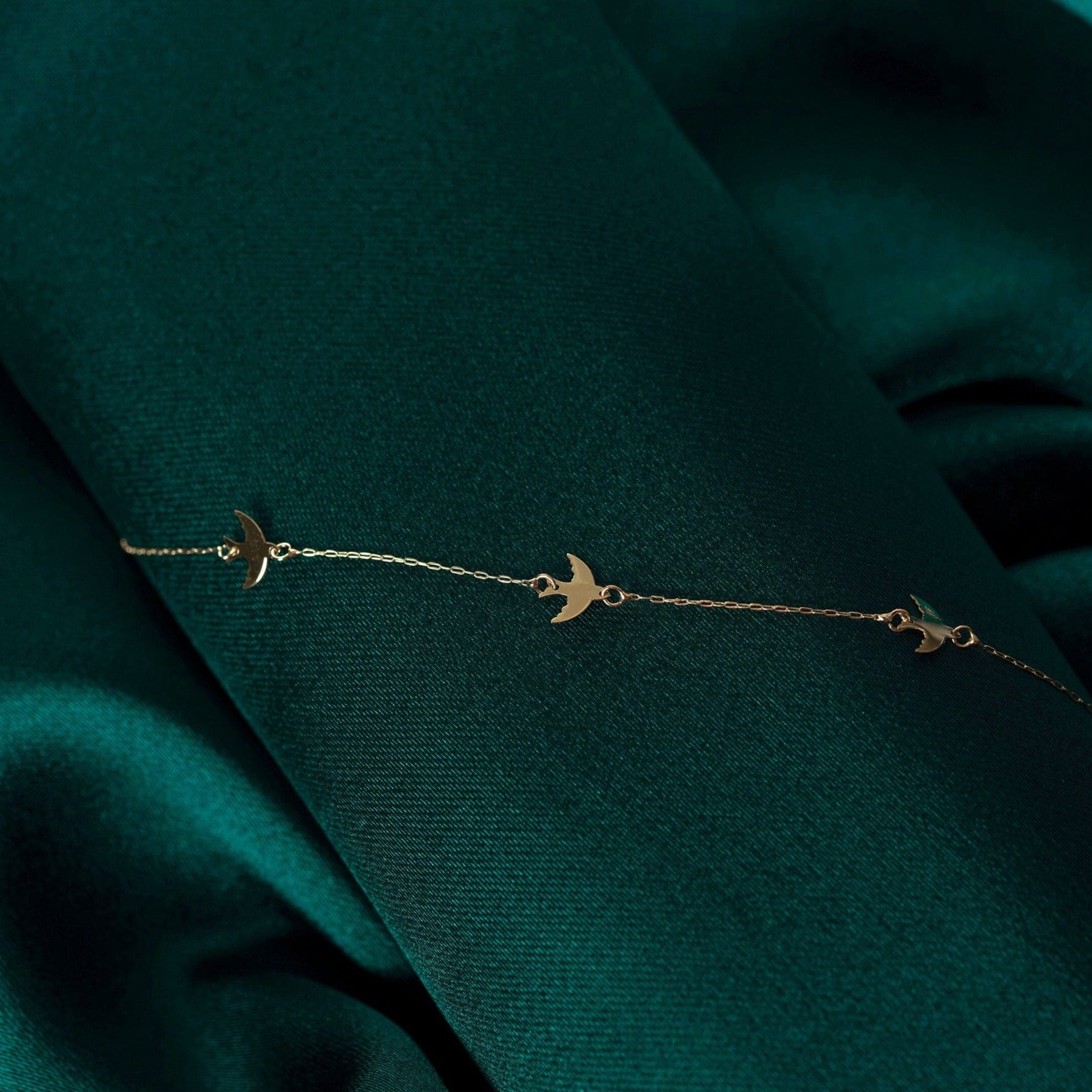 Minimal 14K gold bracelet with flying bird charms on green satin