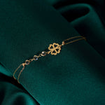 14K gold bracelet with four-leaf clover charm and gemstone details on green satin