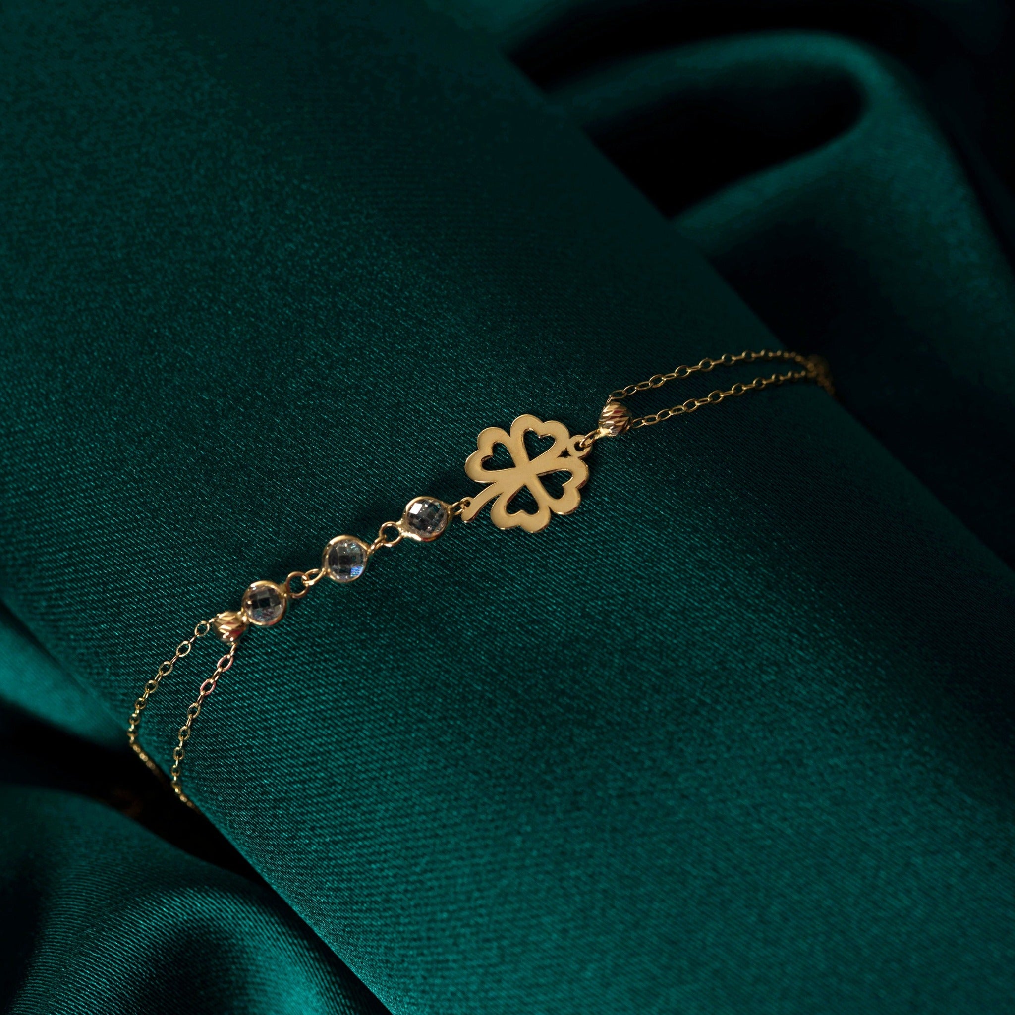 14K gold bracelet with four-leaf clover charm and gemstone details on green satin