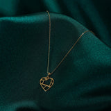 Minimalist 14K gold geometric heart pendant necklace displayed on dark green satin fabric.