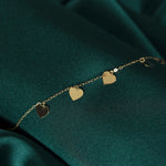 Close-up of 14K gold bracelet with five dangling heart charms on green satin background – perfect for gift-giving or everyday wear