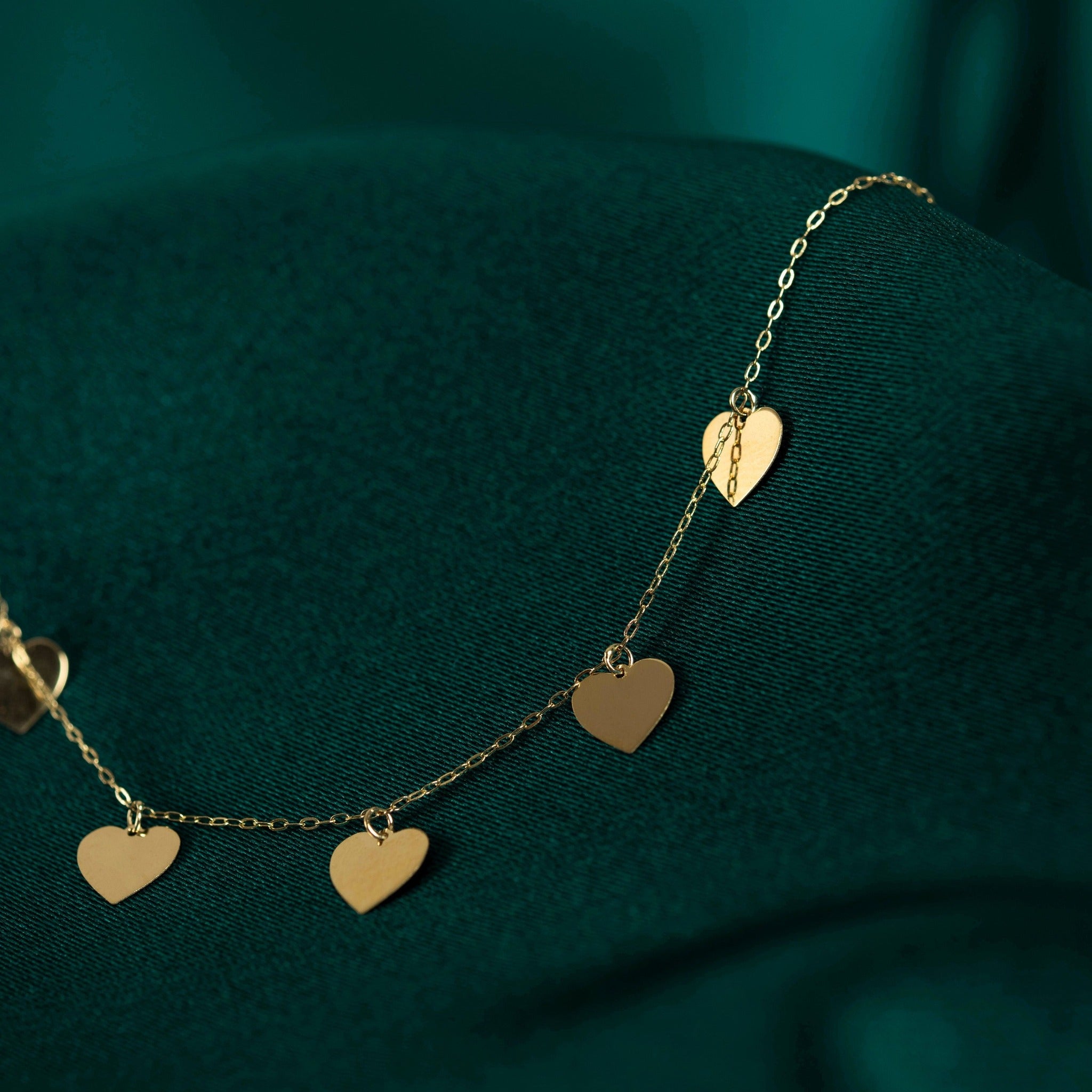Multiple heart charm necklace in 14K gold, styled on rich emerald green fabric, reflecting elegance and affection.