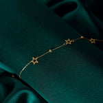 Close-up of a 14K gold bracelet with hollow star charms and gold beads, displayed on dark green satin fabric.