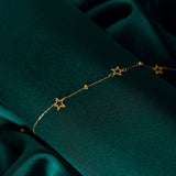 Close-up of a 14K gold bracelet with hollow star charms and gold beads, displayed on dark green satin fabric.
