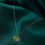 14K gold infinity heart necklace resting on emerald green fabric, symbolizing eternal love and connection.