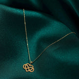 14K gold infinity heart necklace resting on emerald green fabric, symbolizing eternal love and connection.