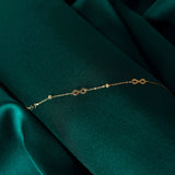 14K gold bracelet with multiple small infinity charms and decorative beads on green background