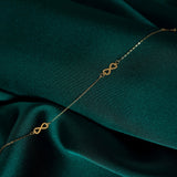 Minimalist 14K gold bracelet with repeating infinity symbols, displayed on emerald green satin