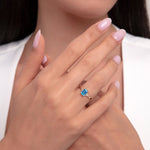 Close-up of a hand wearing a 14K gold ring with a vivid London blue topaz and accent diamonds