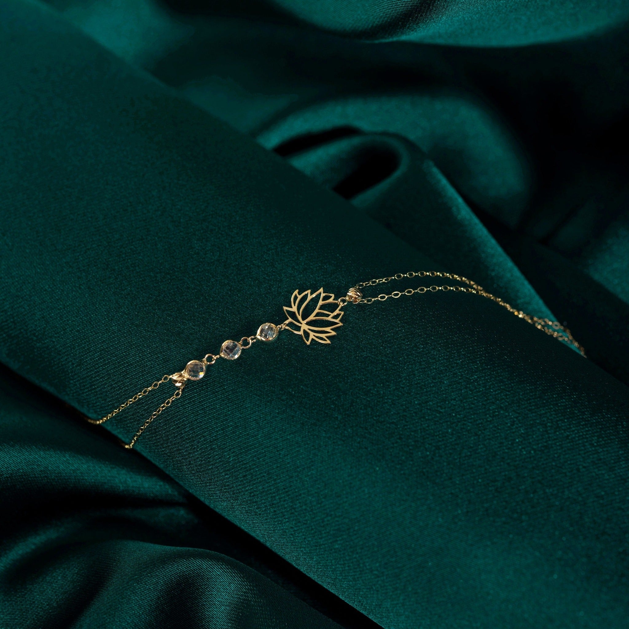 14K gold bracelet with lotus flower charm and faceted gemstone beads on emerald green satin background
