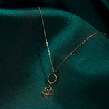Elegant 14K gold necklace featuring a textured circle and a lotus flower pendant, styled on dark emerald fabric.