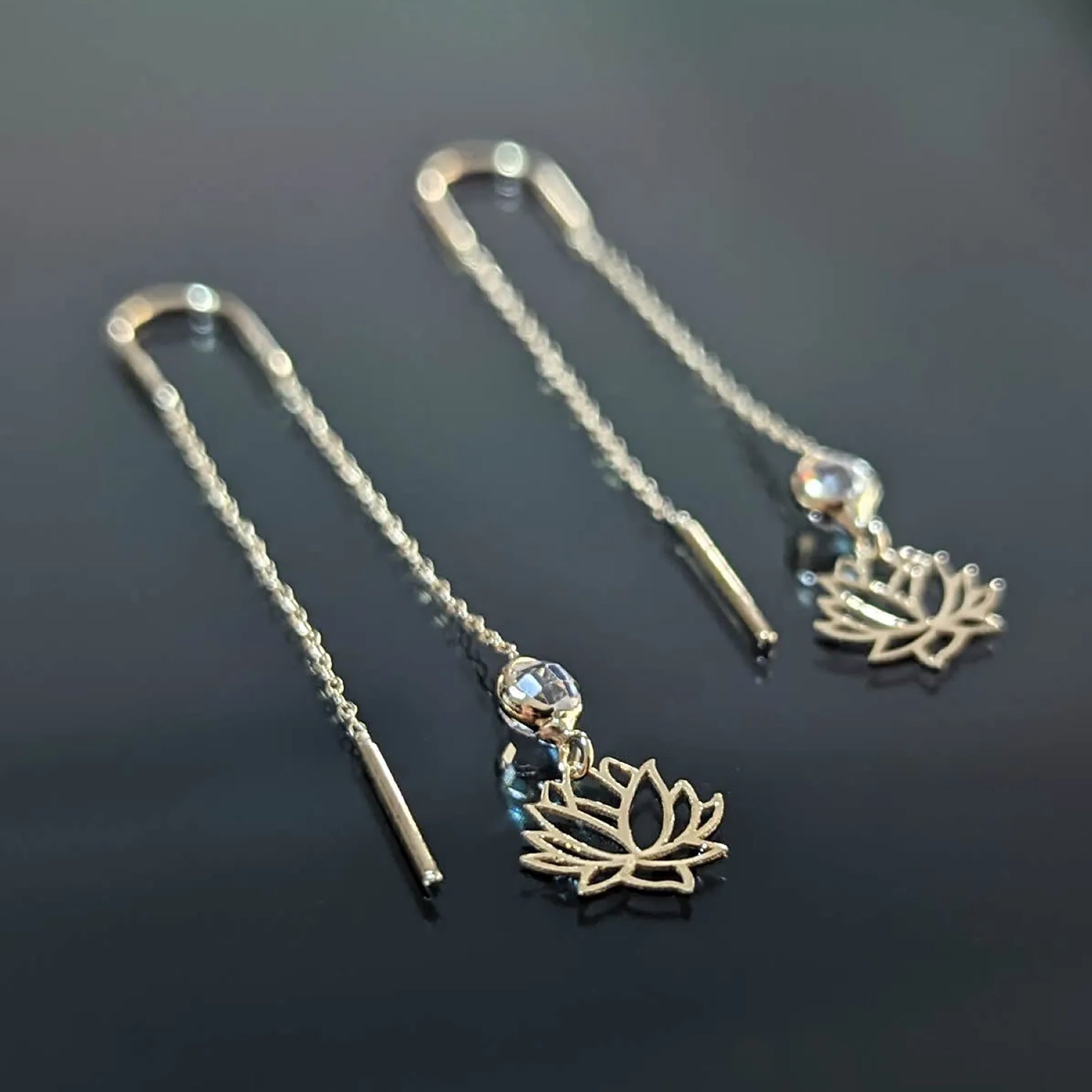 14K gold lotus threader earrings with crystal accents on black background, showcasing spiritual and elegant design