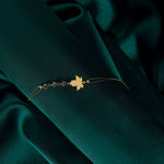 14K gold bracelet with maple leaf charm and gemstone accents on green satin