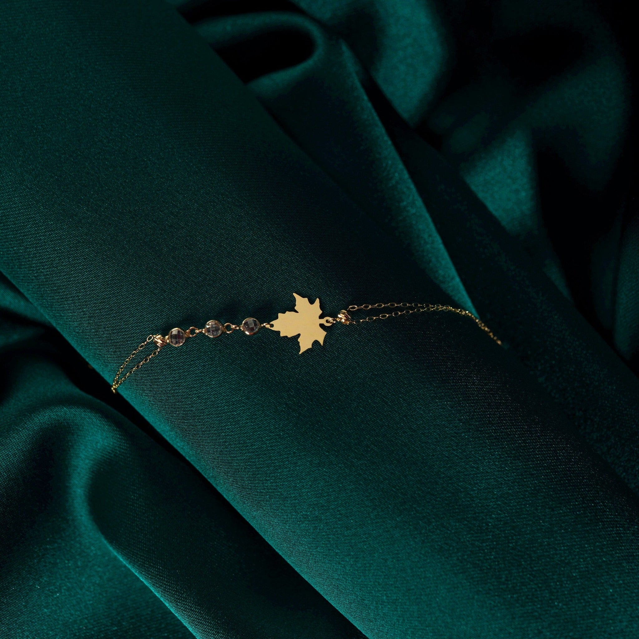 14K gold bracelet with maple leaf charm and gemstone accents on green satin