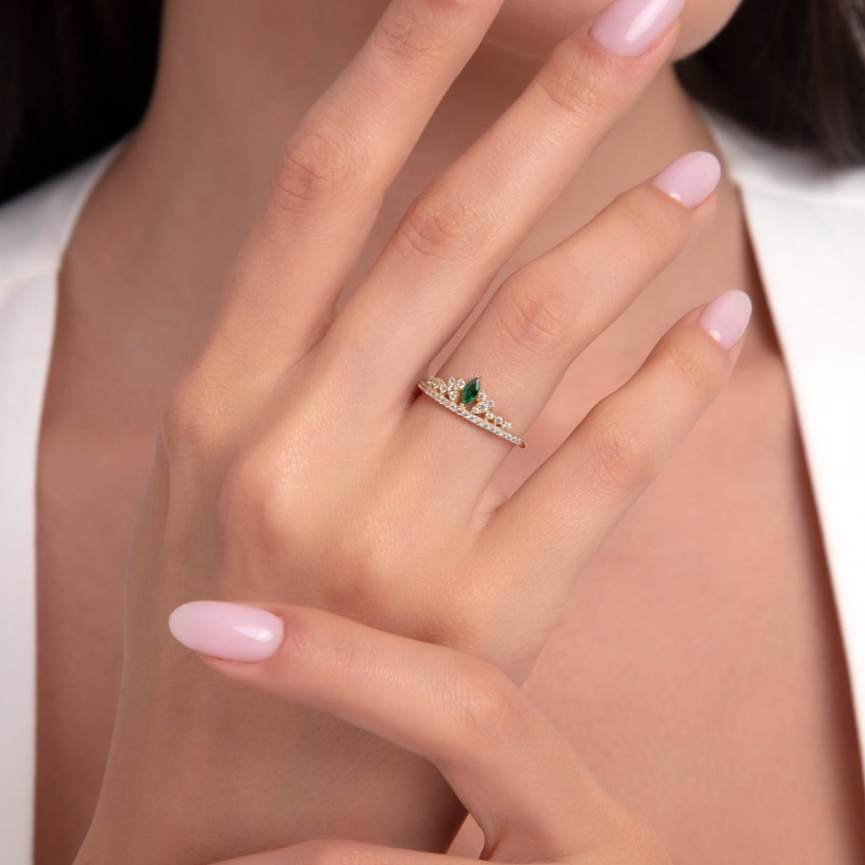 Model wearing a 14K gold ring with marquise emerald stones and white zircons in a crown-leaf design