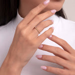 Close-up of a woman's hand wearing a delicate 14K gold eternity band with micro pavé-set diamonds, styled with pastel pink nails and a white ribbed turtleneck.