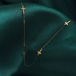 14K gold necklace with multiple small cross charms displayed on dark green satin fabric, elegant and minimalistic.