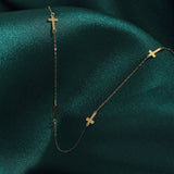 14K gold necklace with multiple small cross charms displayed on dark green satin fabric, elegant and minimalistic.