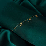 14K gold bracelet featuring five minimalist cross charms, styled on emerald green satin