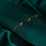 14K gold bracelet featuring five minimalist cross charms, styled on emerald green satin