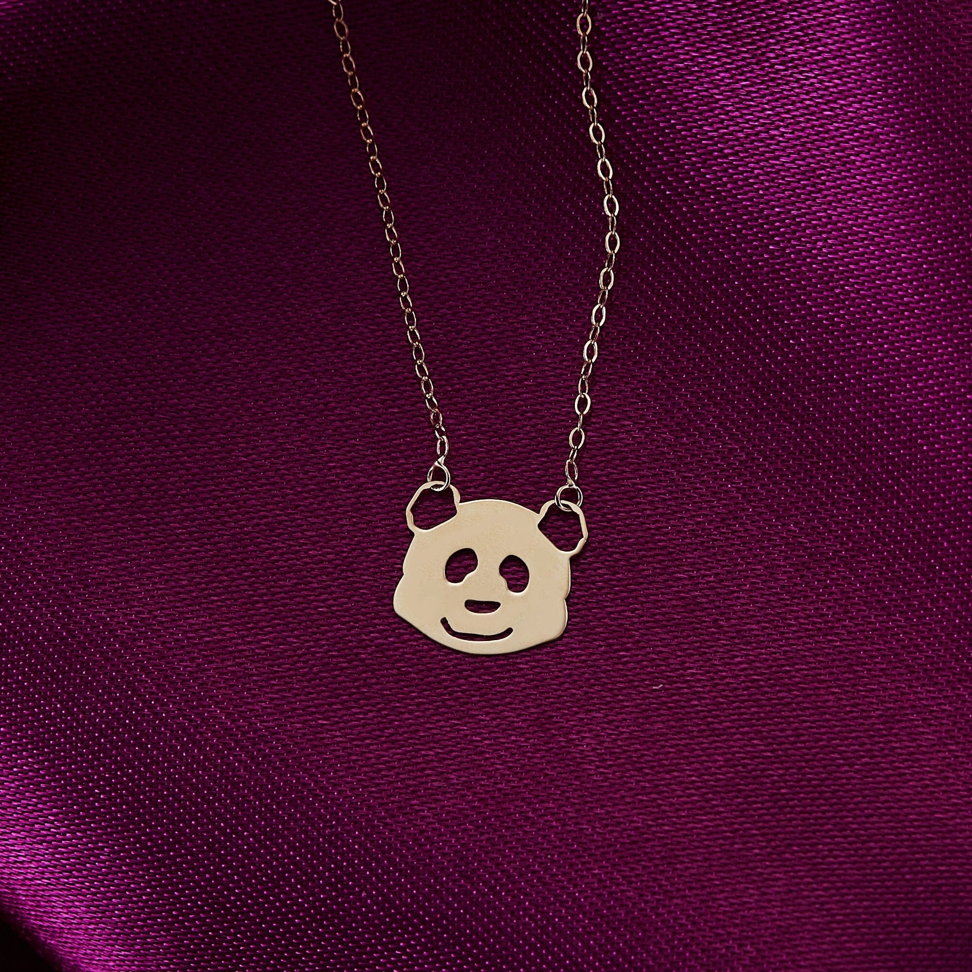 14K gold necklace featuring a smiling panda face pendant on a pink satin background – playful and minimalist jewelry style.
