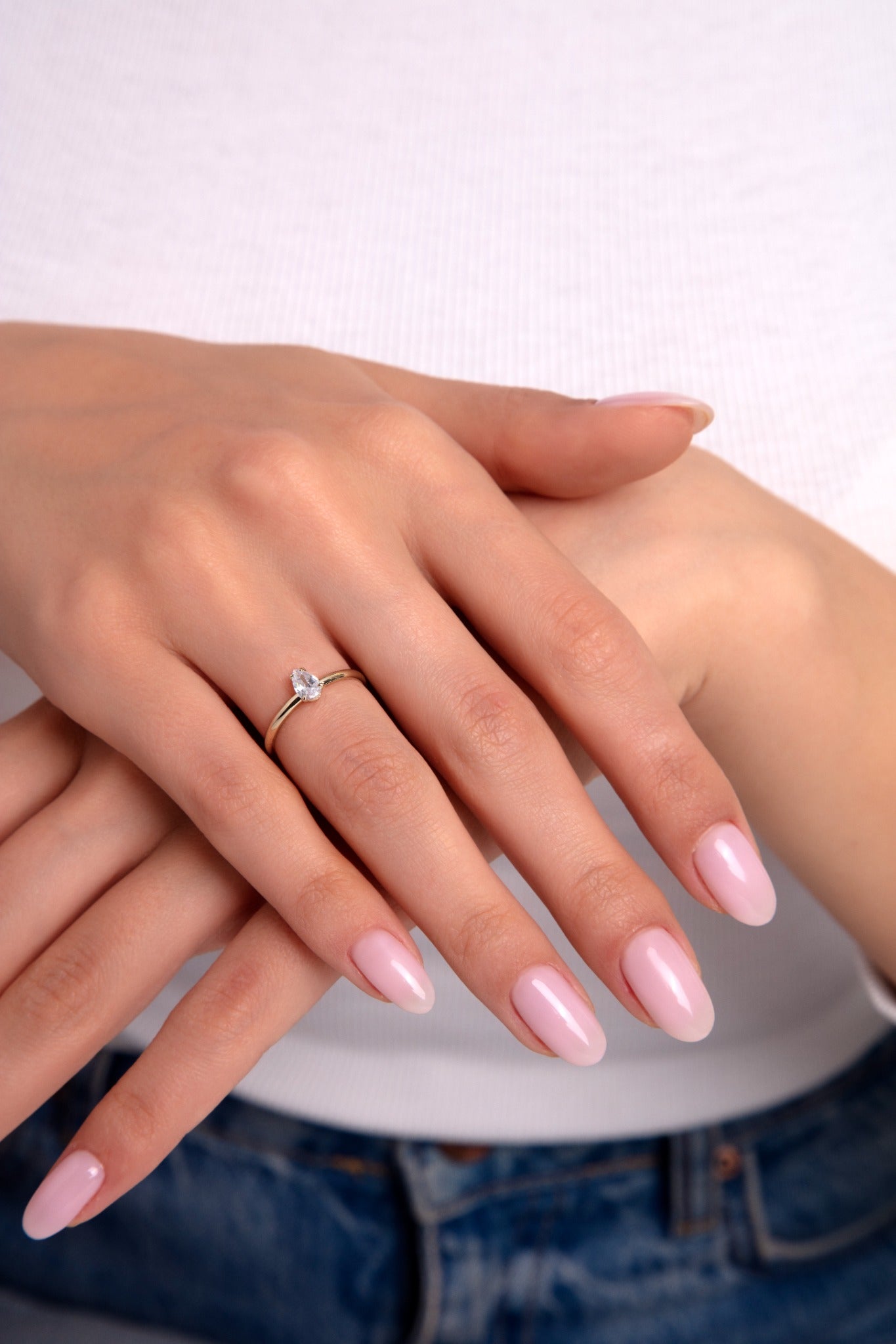 Delicate gold ring with pear-cut solitaire stone on woman’s hand wearing casual jeans, minimalist elegance