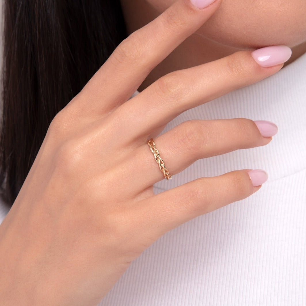 Close-up of a woman's hand wearing a 14K gold rope-style twisted ring with a braided design