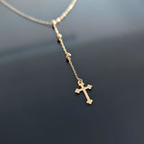 Close-up image of a 14K gold rosary-style necklace with a delicate cross pendant, shot on a sleek black background.