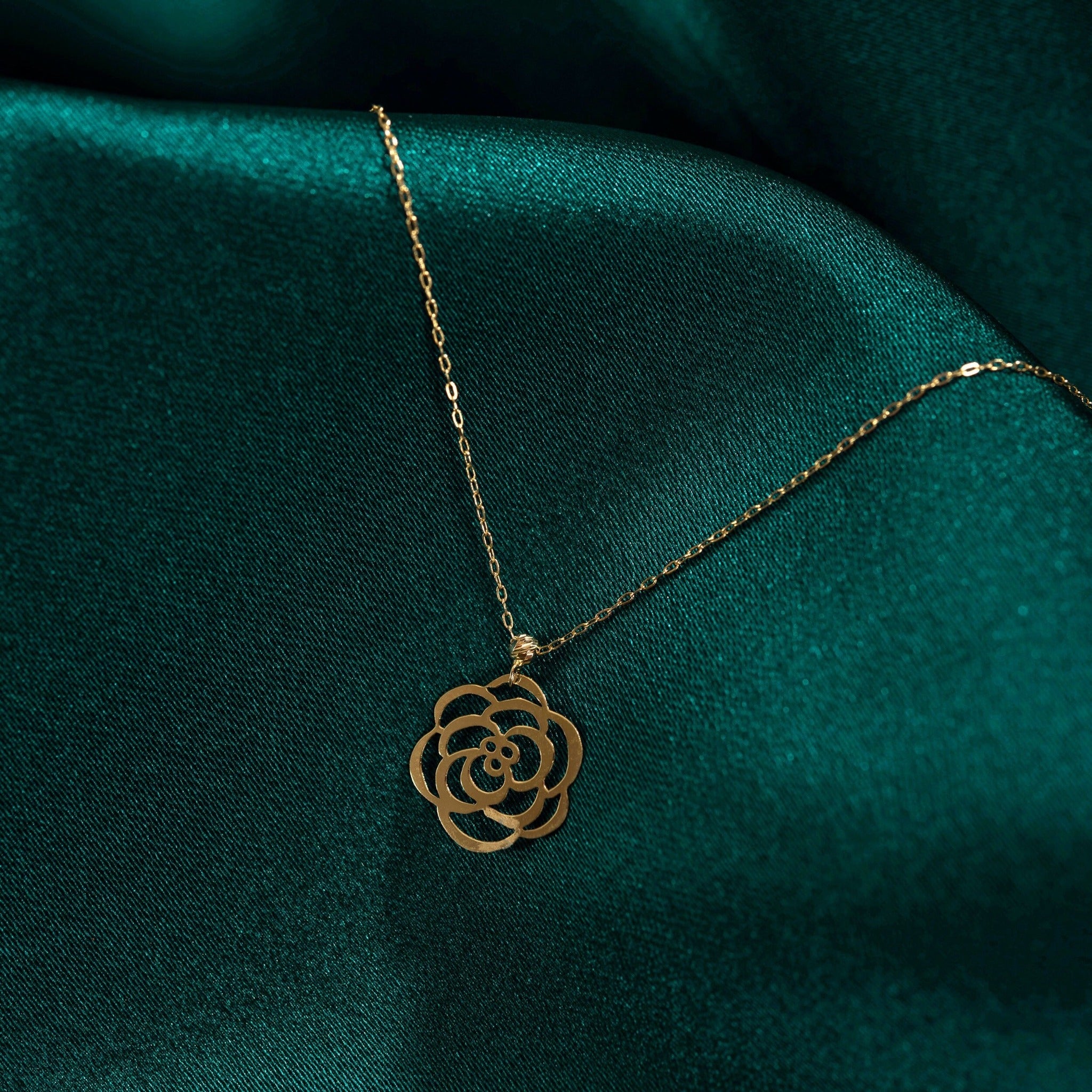 Real 14K gold rose-shaped flower pendant necklace displayed on dark green fabric, symbolizing elegance and love.