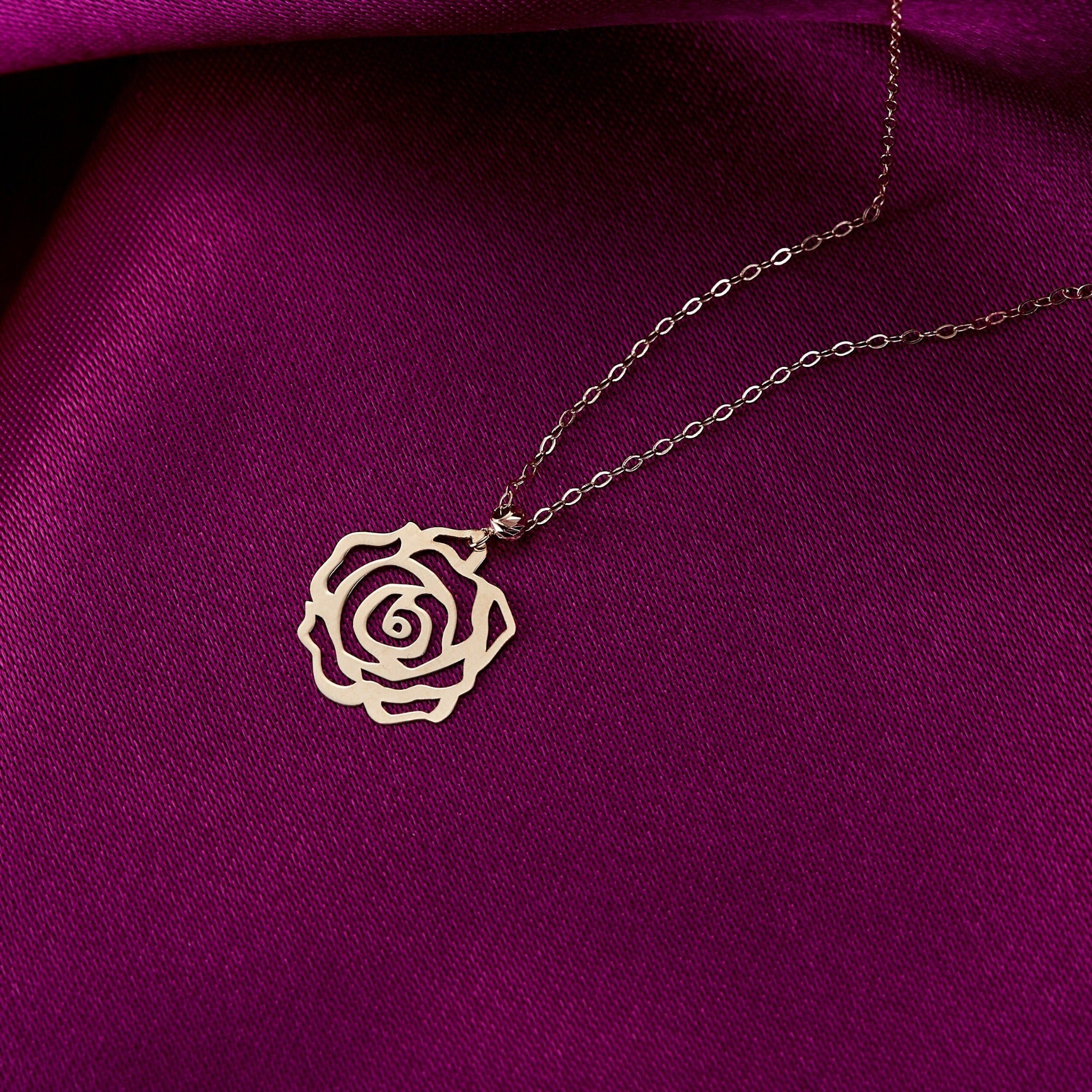 Delicate 14K gold necklace with an openwork rose flower pendant on a vibrant purple fabric background – minimal and elegant floral design.