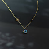 14K gold necklace with teardrop blue sapphire and round gold initial disc charm on a dark background – elegant and minimalist.