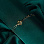 Elegant 14K gold bracelet with a cut-out seashell charm and faceted crystal beads, styled on rich emerald satin