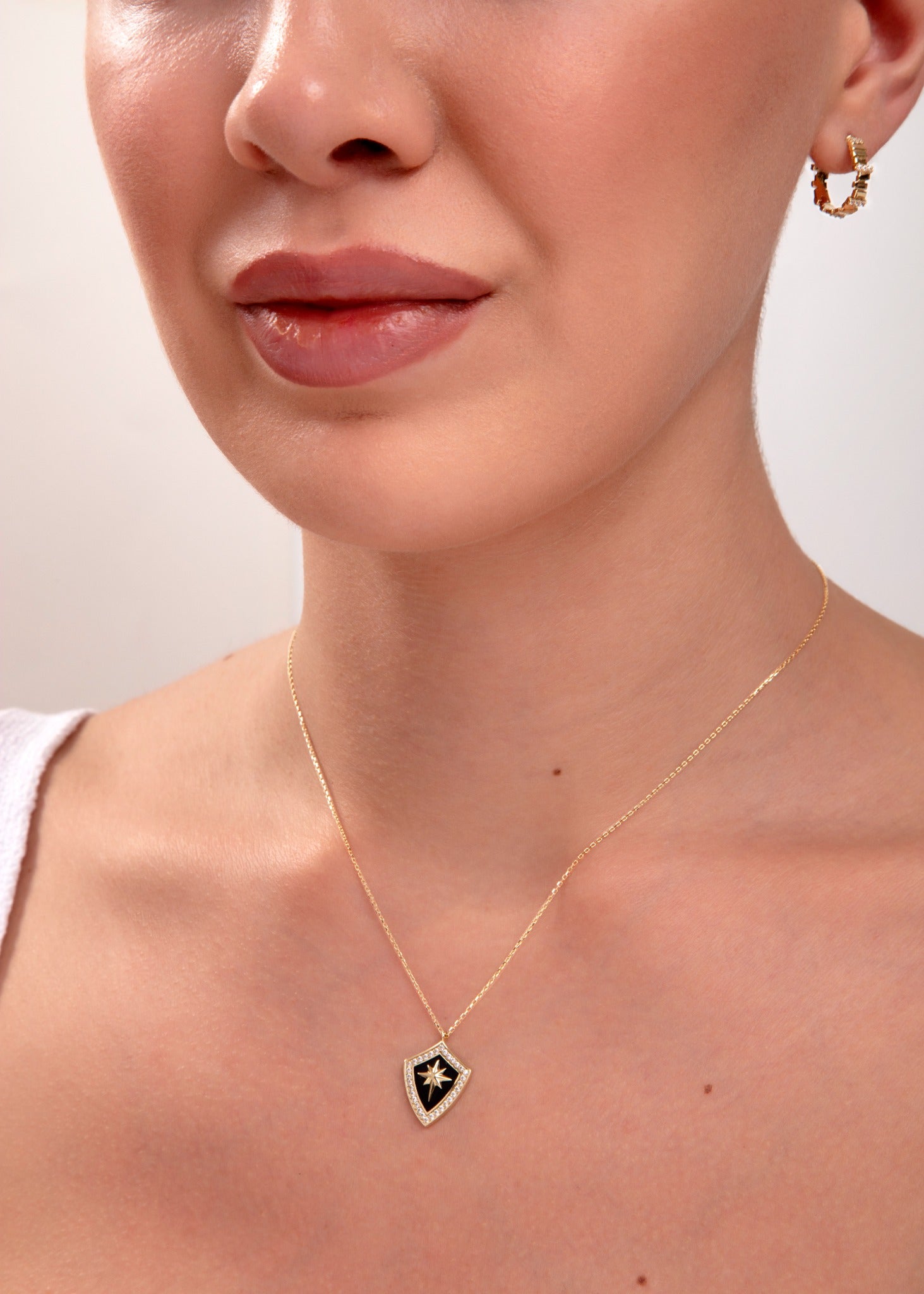 Elegant 14k gold shield pendant necklace with black enamel and star design on a woman’s neck

