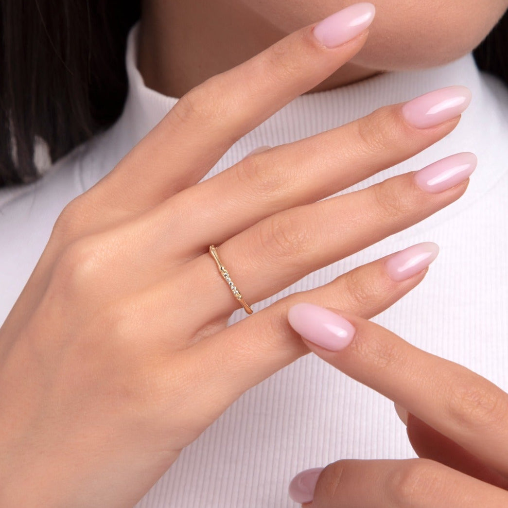 Close-up of a woman wearing a thin 14K gold ring featuring tiny sparkling diamonds, styled on her hand