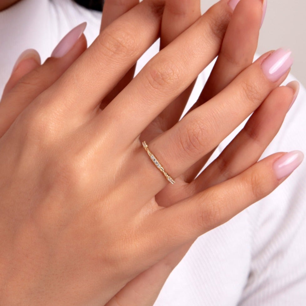 Close-up of a woman's hand wearing a slim twisted 14K gold ring with tiny embedded diamonds