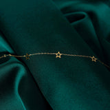 14K gold bracelet with delicate open star charms on green fabric