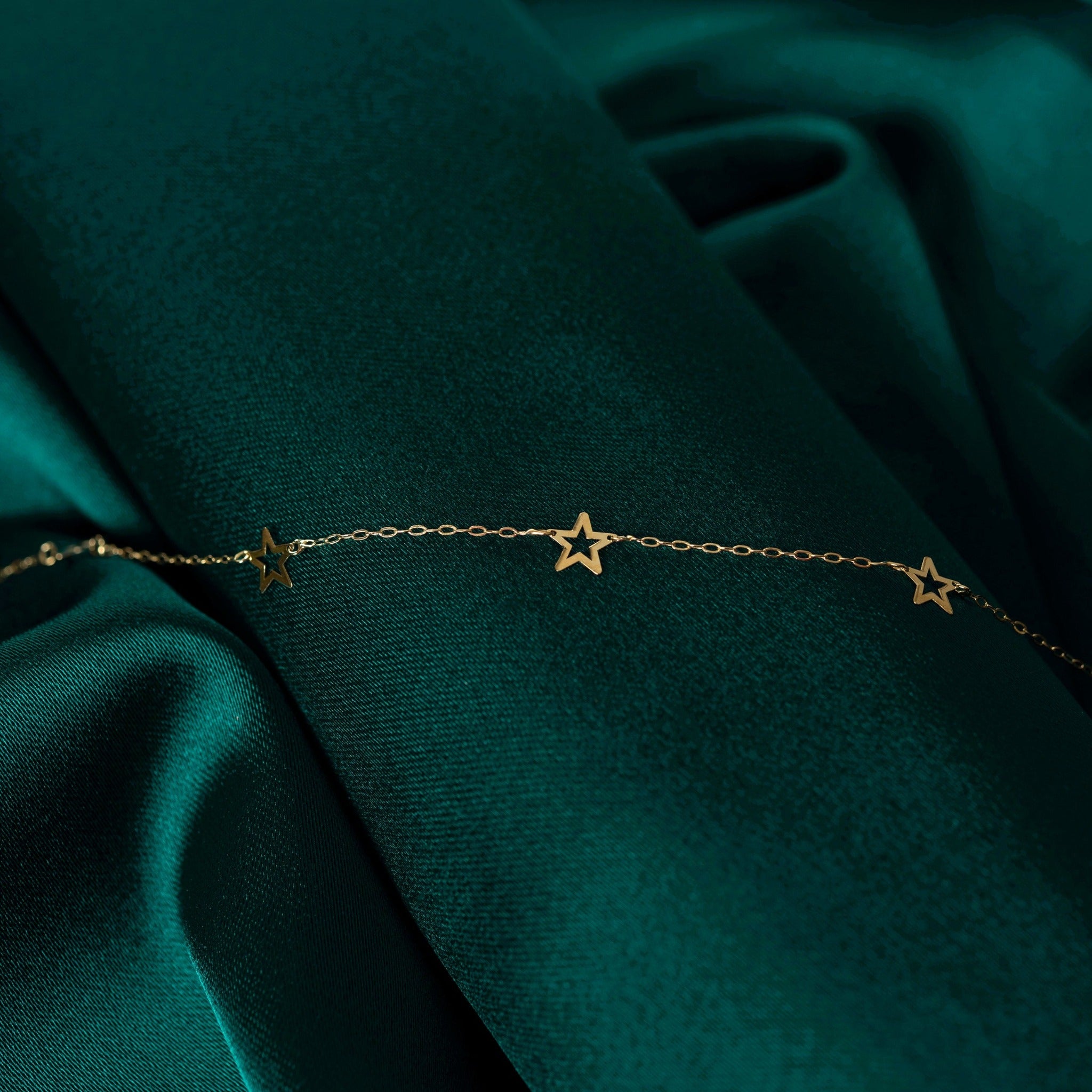 14K gold bracelet with delicate open star charms on green fabric