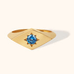 14K gold signet ring with starburst engraving and blue gemstone, celestial inspired jewelry on cream background.