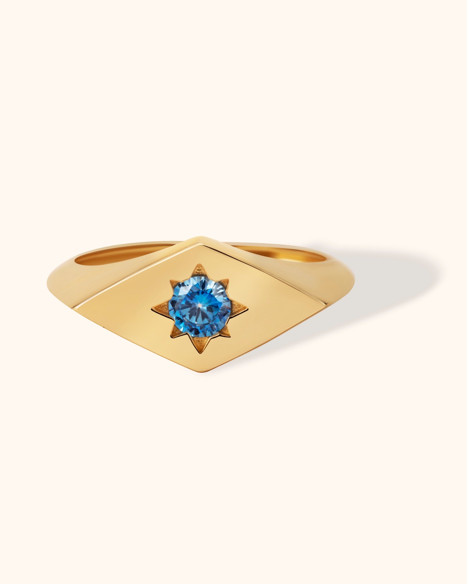 14K gold signet ring with starburst engraving and blue gemstone, celestial inspired jewelry on cream background.
