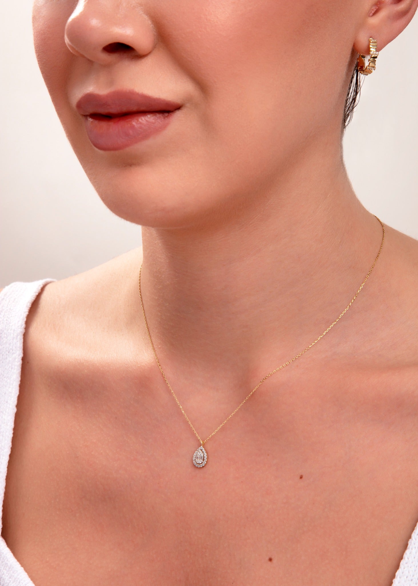 Close-up of woman wearing 14k gold teardrop necklace with pavé halo cubic zirconia pendant

