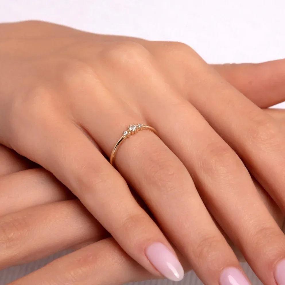 Close-up of a delicate 14K gold ring featuring three clustered diamonds, worn on a woman's hand with soft pink nails, resting gently over the other hand.