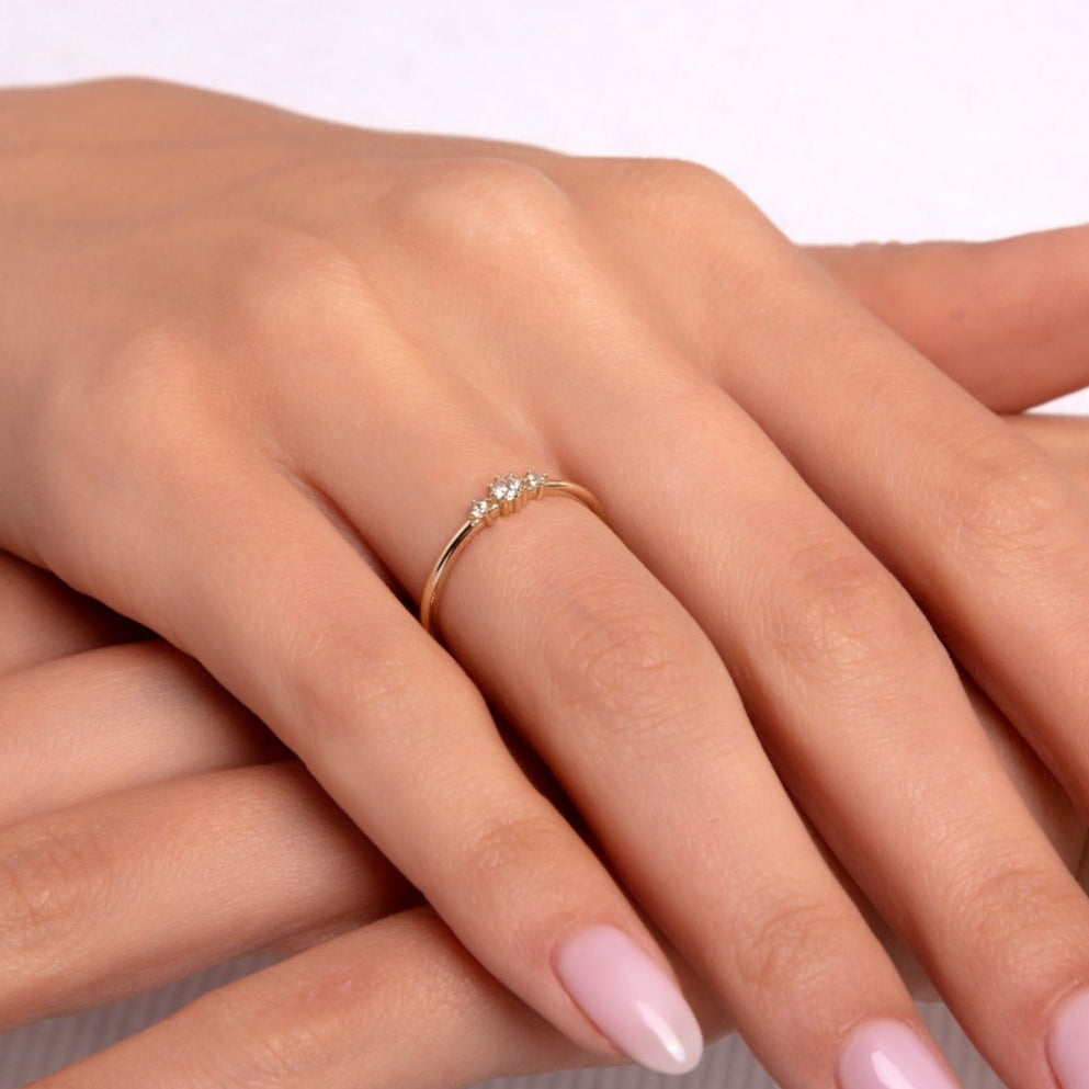 Close-up of a delicate 14K gold ring featuring three clustered diamonds, worn on a woman's hand with soft pink nails, resting gently over the other hand.