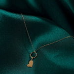 14K gold tilted heart necklace with textured loop, displayed on green satin fabric, minimalist romantic jewelry.