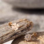 14K Gold Tragus Piercing Pair featuring a polished four-leaf clover stud and a sparkling CZ daisy flower stud – Charming cartilage earrings symbolizing luck and radiance, perfect for tragus or helix piercings."