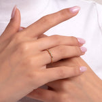 Delicate 14K yellow gold ring with three small diamonds, worn on a woman's hand with light pink manicure, against a white turtleneck background