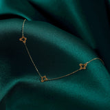 Minimalist 14K gold necklace with three evenly spaced clover charms, set on emerald green satin fabric for an elegant look.