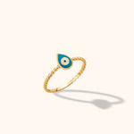 Close-up of a delicate 14K yellow gold beaded band ring featuring a turquoise enamel evil eye motif against a neutral background.